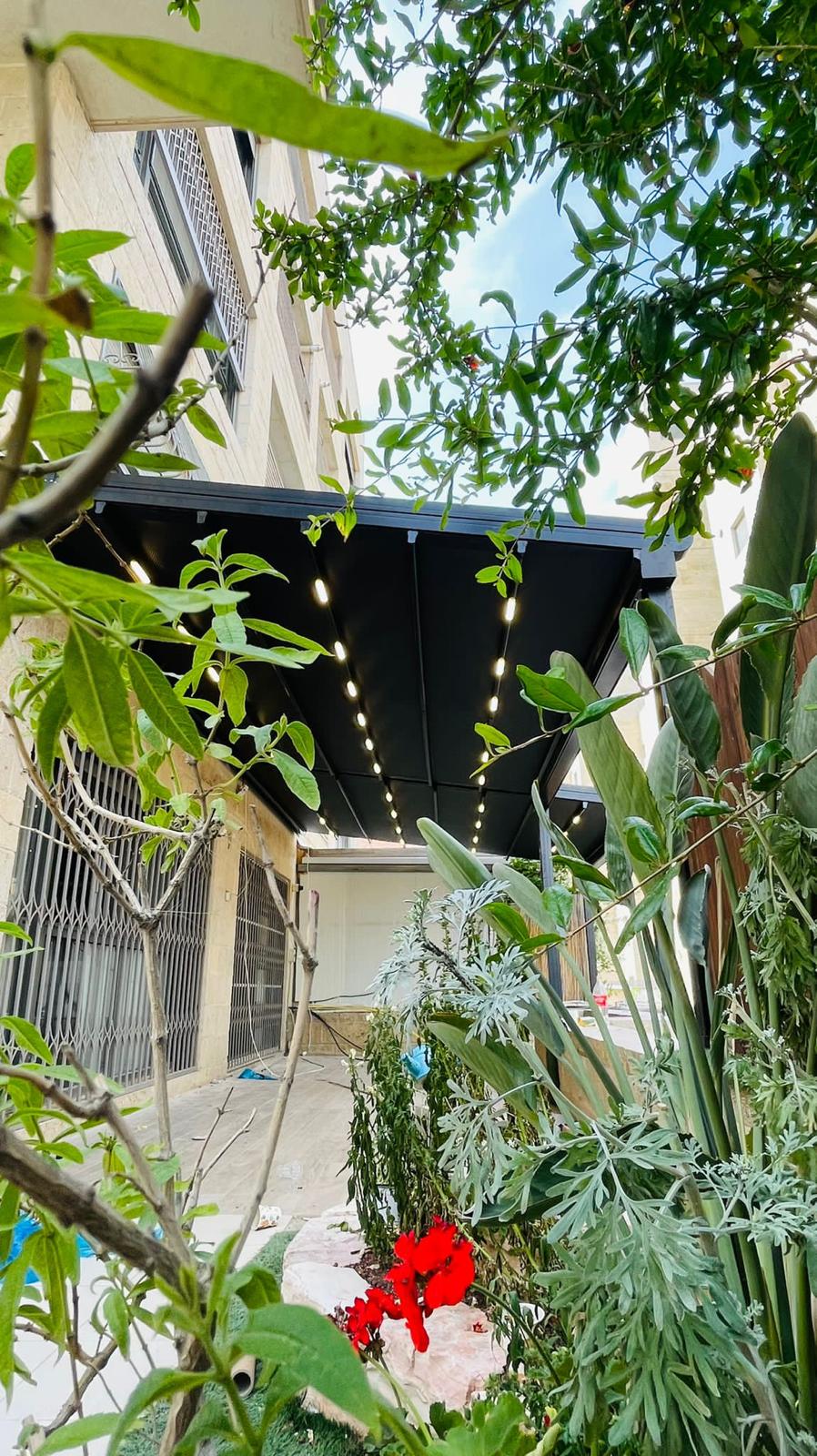 פרגולת אלומיניום שחורה עם תאורת LED בגינה פורחת